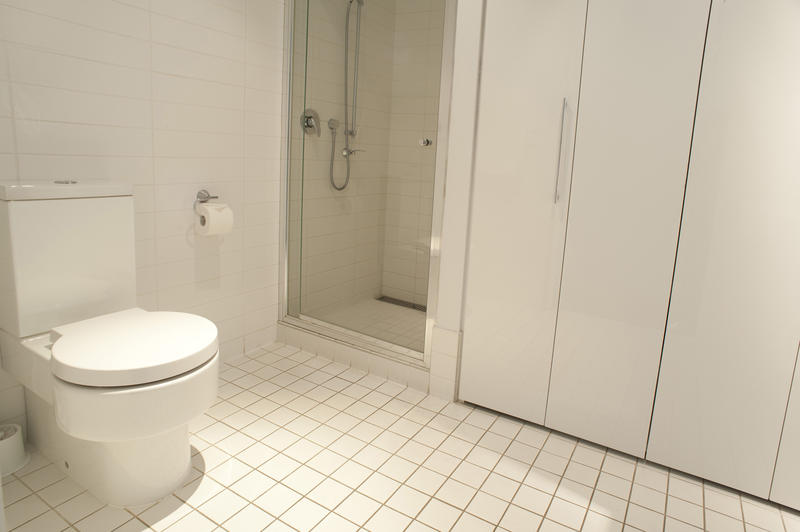 Monochromatic white bathroom interior with a white toilet, cabinets and shower cubicle over a white tiled floor