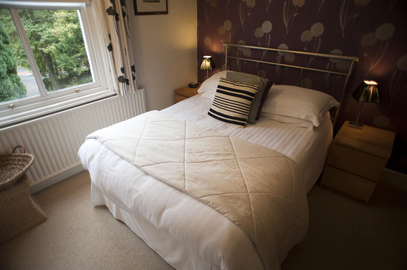 Cosy bedroom with a fresh white bed set on a classical wrought iron bed overlooked by a window with a view of a leafy green garden