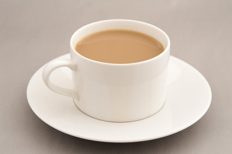 Cup of coffee with milk on saucer standing on grey table
