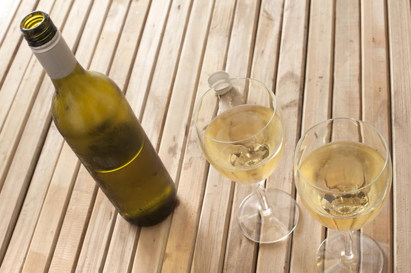 Serving of chilled white wine in two wineglasses alongside an unlabelled bottle on a slatted wooden table, high angle view