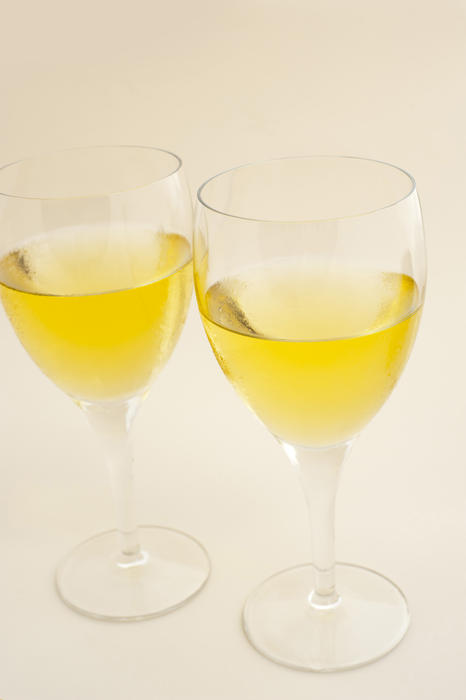 Two glasses of white wine standing side by side on a pale yellow background conceptual of relaxation, aperitif and entertainment