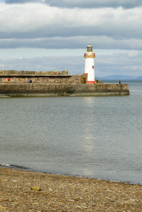 View from the beach of the Whitehaven harbour seawall topped by a lighthouse with a beacon to guide incoming shipping