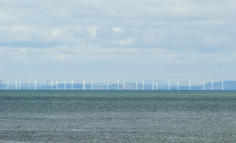 View across a calm ocean of a row of wind turbines in an offshore windfarm generating power and electricity from the kinetic energy of the wind