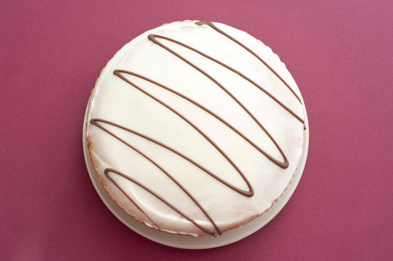 Freshly backed glazed cake with a decorative zigzag pattern on the icing viewed overhead on a festive red background