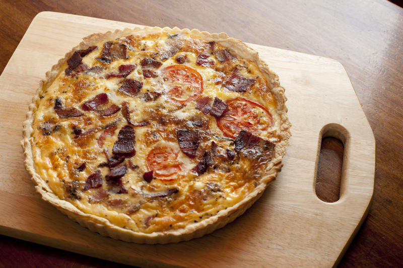 Whole delicious freshly baked savoury quiche in a crisp golden pie crust standing on a wooden board, high angle view