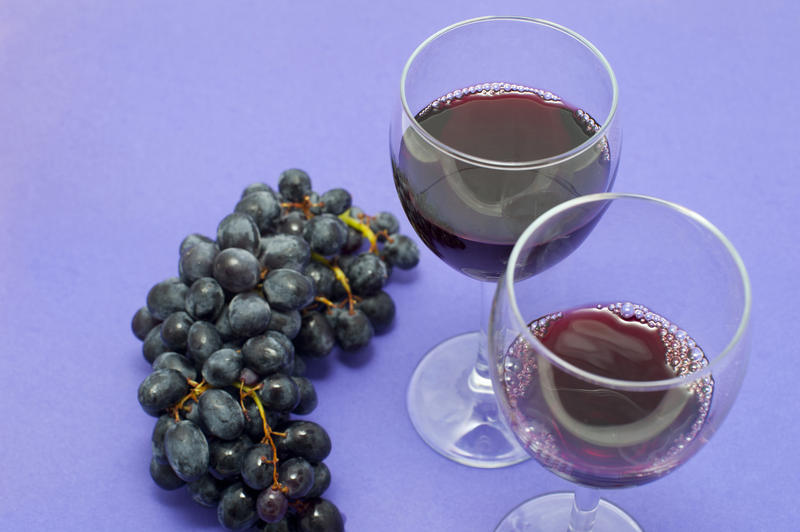 Close Up of Bunch of Dark Red Grapes on Purple Studio Background Next to Full Empty Wine Glasses with Copy Space