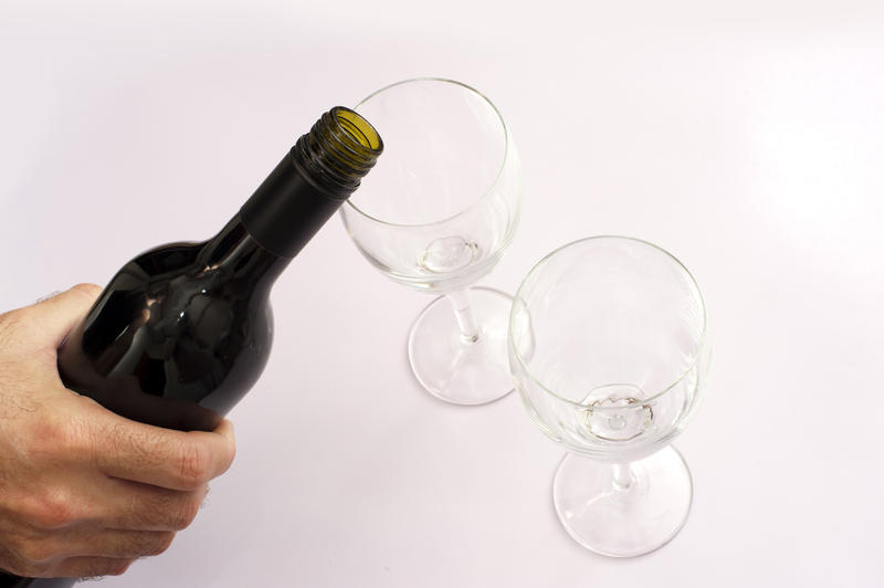 Male hand serving wine from a bottle into two clean glasses, high-angle close-up on grey