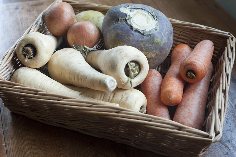 Fresh root vegetables in a wicker basket at market including carrots, parsnip, turnip and onions