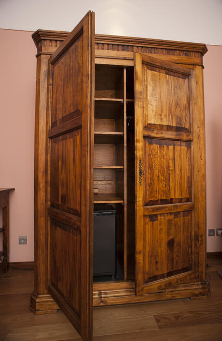Old wooden wardrobe or armoire standing with its doors ajar revealing the empty shelves inside for storage of clothing or household goods