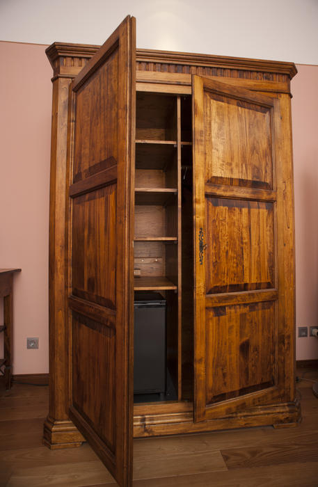 Old wooden wardrobe or armoire standing with its doors ajar revealing the empty shelves inside for storage of clothing or household goods