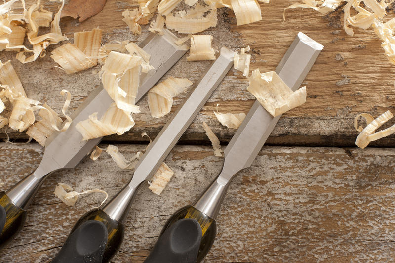 Set of three woodworking chisels lying on rustic wooden boards with fresh wood shavings in a carpentry or woodworking concept