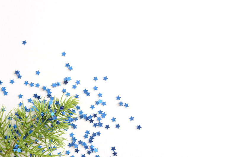 Festive Christmas background with blue stars and a sprig of fir foliage over a white background with copyspace for your greeting or invitation
