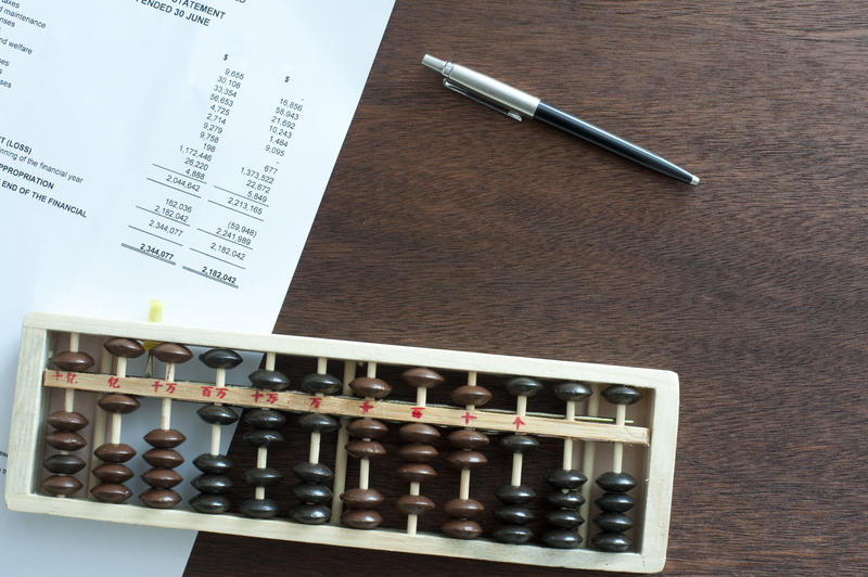 Short wooden rectangular abacus on table beside two toned executive pen and a printed income statement