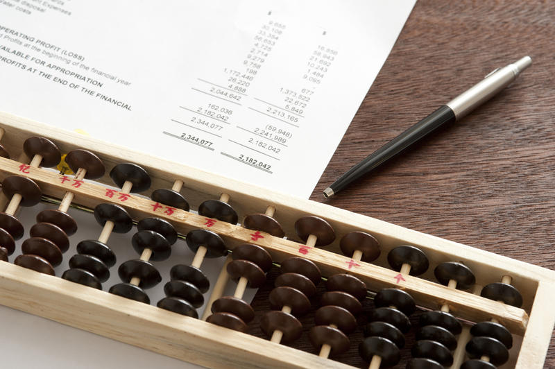 Business balance sheet with abacus and pen lying on a wooden desk in an accounting concept