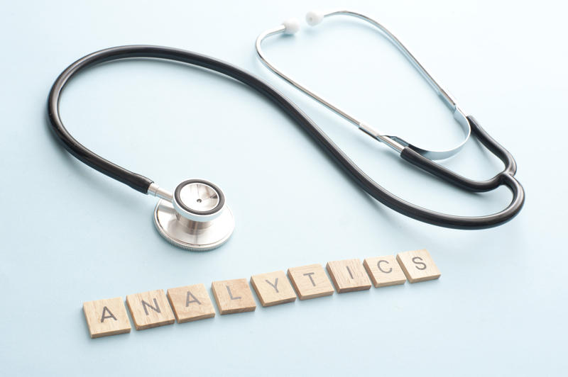 Analytics expertise concept with laid out medical stethoscope and simple wooden block letters over blue background