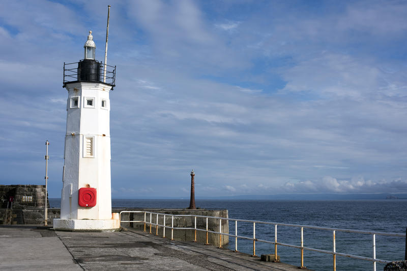 Lighthouse on the pier at the entrance to Anstruther Harbour, Scotland with a second beacon visible in the distance on the other wall on a calm hazy cloud day
