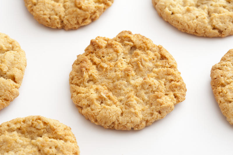 Fresh homemade Anzac biscuits with rolled oats and coconut arranged spread out on white with focus to the centre biscuit