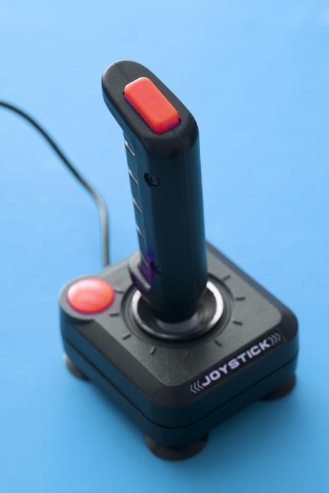 Arcade joystick of black plastic with red control buttons and wire close-up on plain blue background