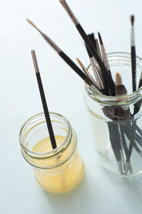 Single brush in cloudy water wash next to taller jar of various dry paintbrushes