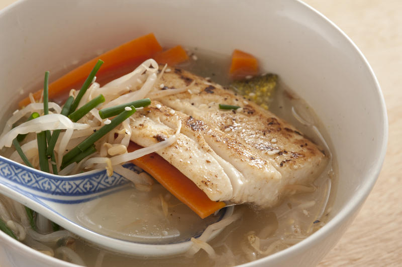 Close up on Asian fish soup filled with warm tasty green chives, bean sprouts and carrot slices over blue and white spoon in bowl