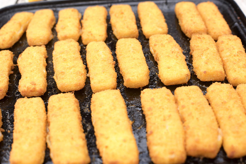 Three rows of freshly baked breaded fish fingers in pan for theme about easy to prepare food