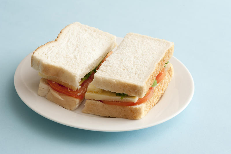 Basic white bread sandwich with cheese and tomato halved and served on a plate over a blue background