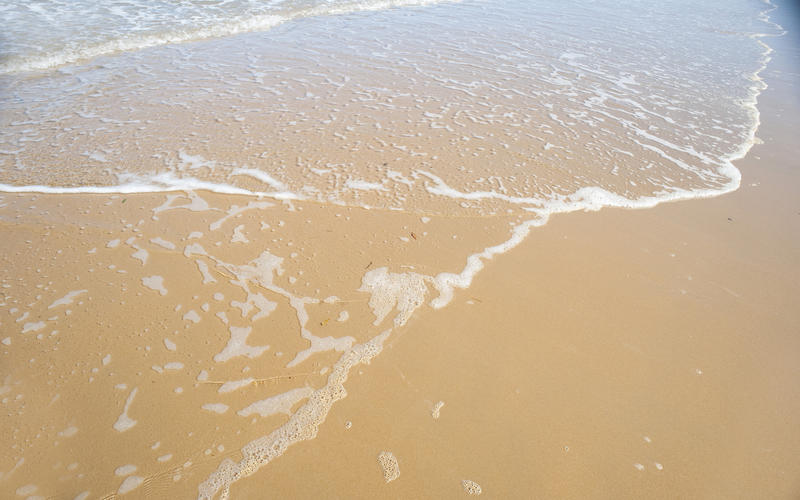 Top down view on foam from wave on smooth sandy beach as water in nature concept background