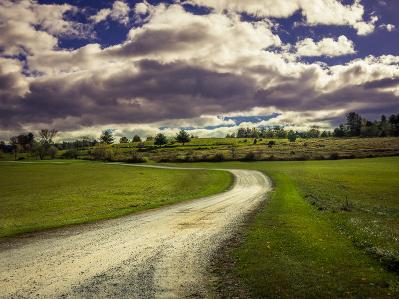 <p>Winding dirt road on a sunny day with big clouds.</p>
