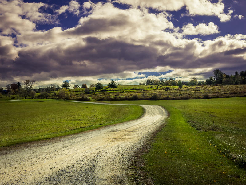 <p>Winding dirt road on a sunny day with big clouds.</p>
