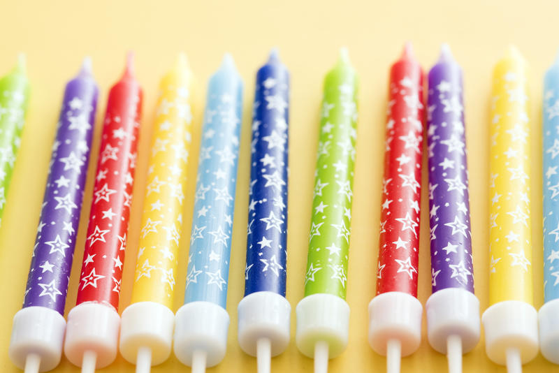 Colorful row of birthday cake candles in the colors of the rainbow decorated with festive stars on a yellow background