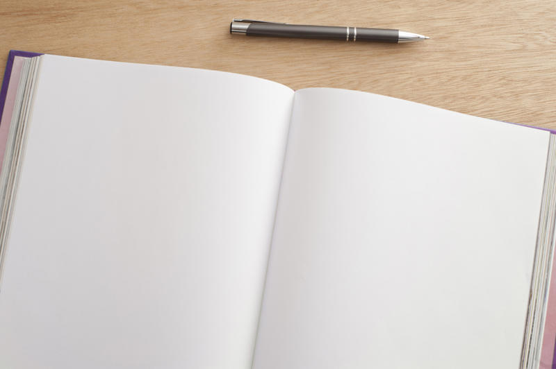 Double spread open blank pages in a journal with a pen above viewed from above on a wooden desk, with copy space