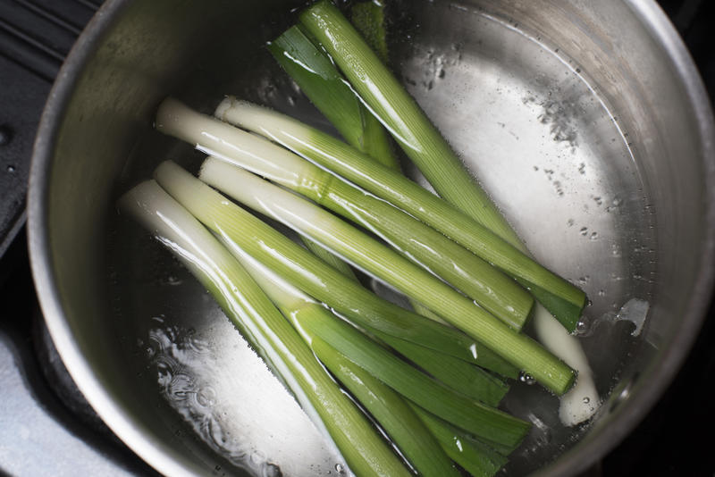 Overhead view of a pot boiling with water and half a dozen green onions cut at both ends