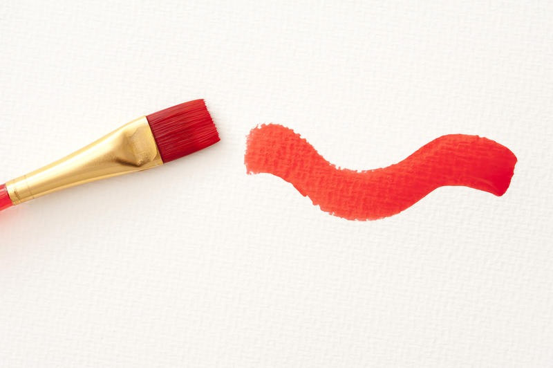 Single plastic and copper paint brush with red curving stroke over textured white paper