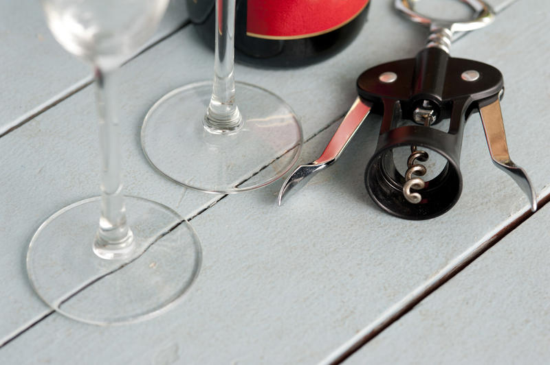 Bottle opener with wineglasses and bottle of wine on a white wooden slatted table with copy space