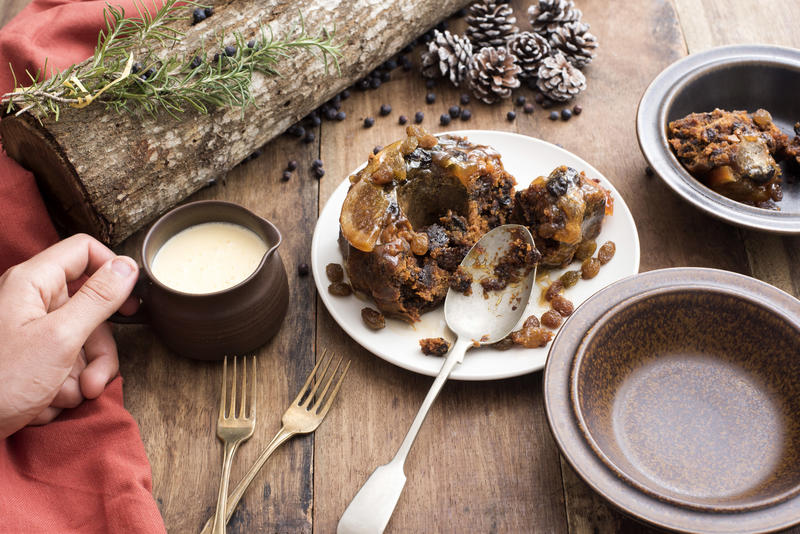 Person serving brandy sauce with a traditional Christmas plum pudding served in pottery bowls on a decorated table