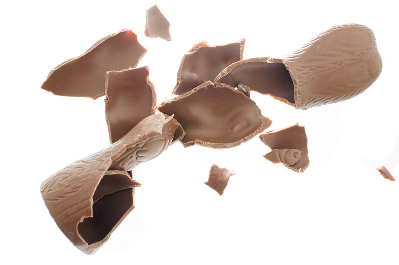 Close-up of cracked chocolate Easter Bunny candy with pieces all around isolated on white background