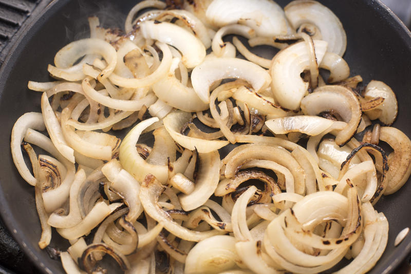 Browning fresh diced white onions in a frying pan, close up overhead view on a griddle