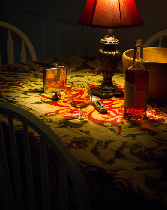 <p>Bottle of Bourbon, a knife, a snifter on a dining room table in a relaxed atmosphere. </p>