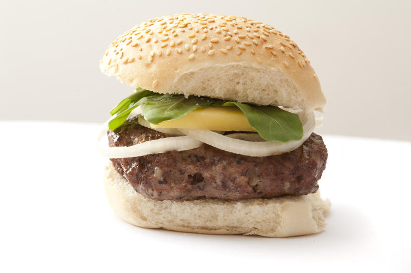 Fat homemade oddly shaped hamburger patty on a seeded bun with onion slices, cheese and lettuce leaves