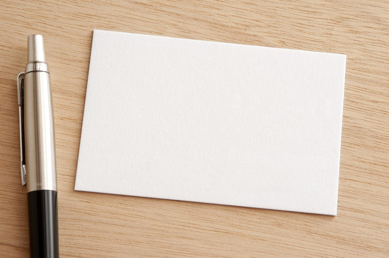 Blank white business card with a ballpoint pen alongside on a wooden background viewed close up from above