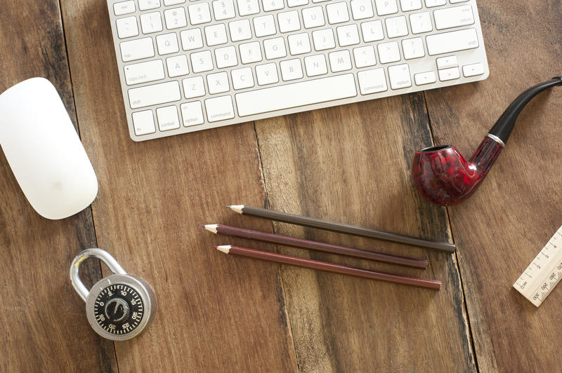 High Angle View of Wooden Desk Scattered with Supplies - Mac Keyboard and Mouse on Desk with Lock, Pencils and Pipe