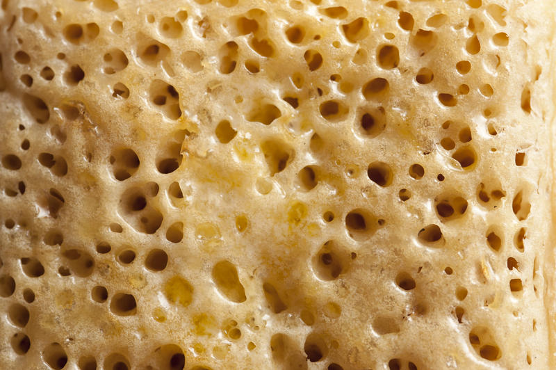 Extreme close up on dozens of air pockets from frying on crumpet coated with melted delicious yellow butter