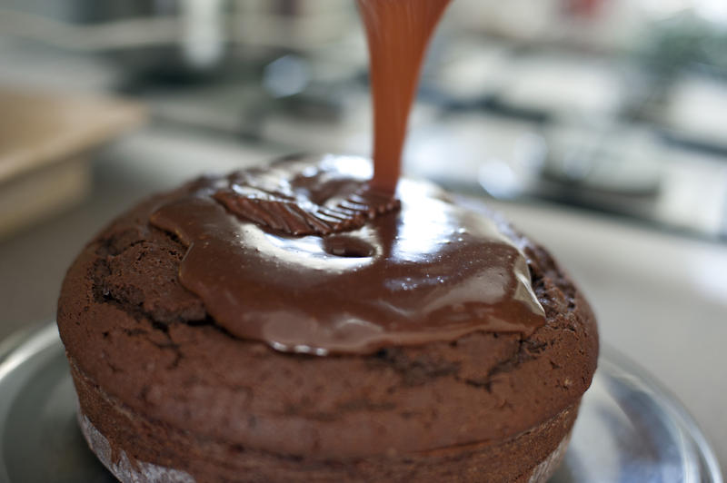 Pouring melted icing onto a freshly home baked chocolate cake in a close up view