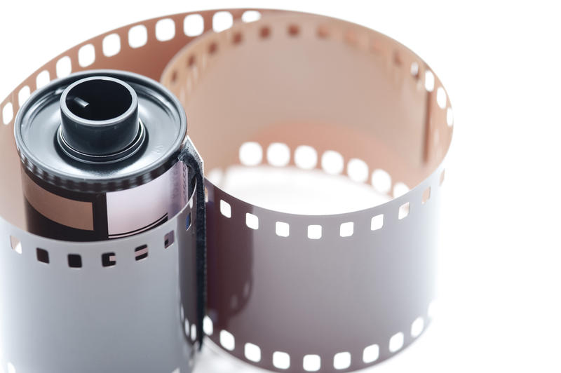 Close Up Still Life of 35mm Film Cannister with Exposed Film Unfurling on White Background with Copy Space - Film and Photography Concept Image