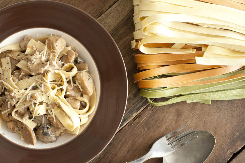 Carbonara Italian pasta with ham, grated cheese, sauce and seasoning in an overhead view with dried noodles alongside