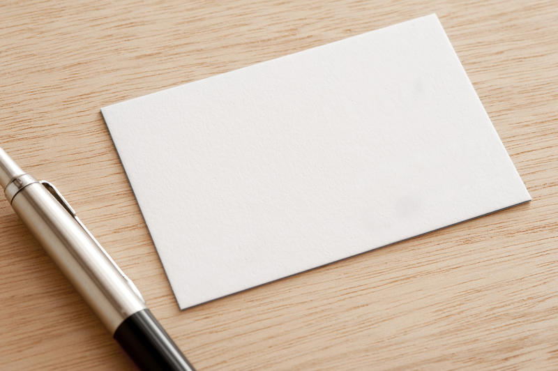Blank white card with a ball point pen lying on a wooden desk with copy space for your text