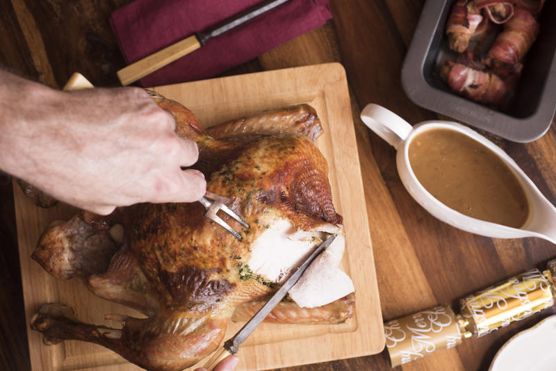 Man carving the Christmas roast turkey for dinner in an overhead view of him slicing breast meat with gravy and bacon rolls alongside