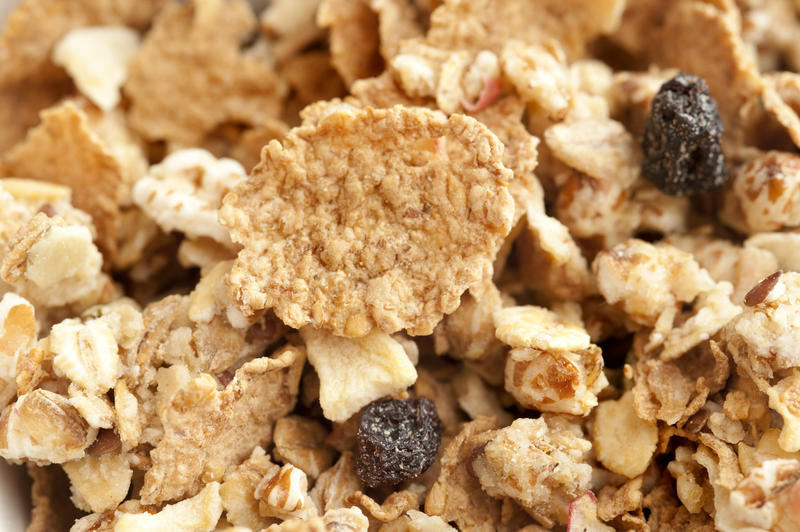 Extreme close up on wheat granola breakfast cereal pieces with chopped nuts and little dry raisins