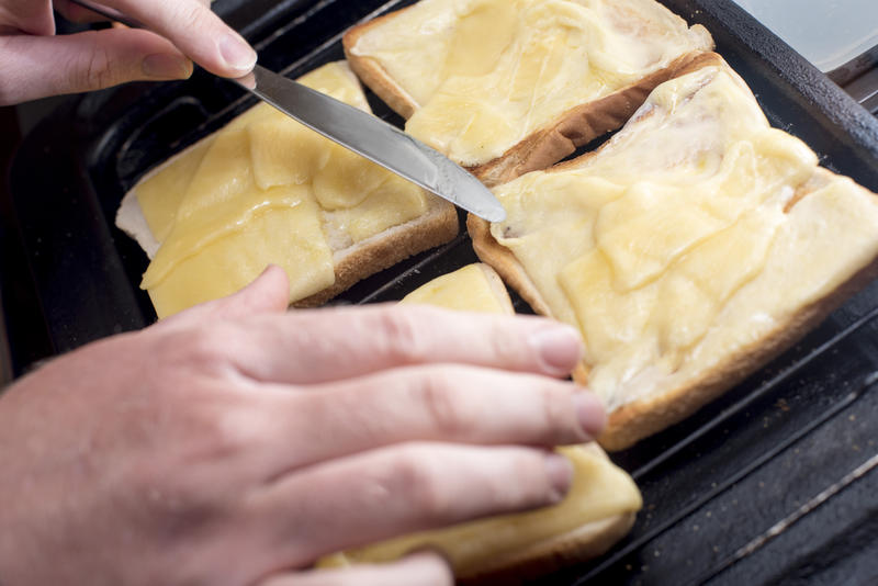 Hands with blunt knife handle toast and cheese melting on four slices of white bread on grill
