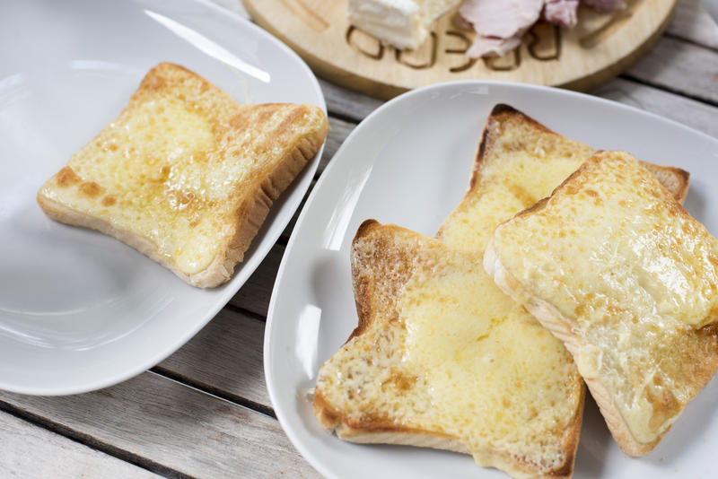 Four square shaped slices of toasted bread and melted mozzarella cheese on top in square plates with round corners